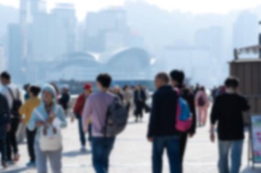 Hong Kong, Çin 'de bir rıhtım boyunca yürüyen insanların bulanık bir görüntüsü. Arka planda şehrin ufuk çizgisi ve Victoria Limanı görünüyor..
