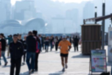 Hong Kong 'da bir rıhtım boyunca yürüyen ve koşan insanların bulanık bir görüntüsü..