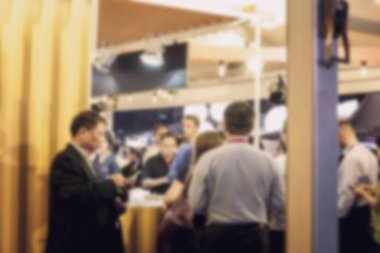 Aydınlık bir odada masanın etrafında duran bir grup insanın bulanık görüntüsü. Arka plan bulanık ve bokeh etkisi var.