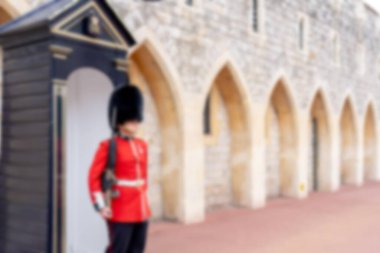 Kırmızı üniformalı bir İngiliz muhafızın bulanık görüntüsü ve taş bir binanın önünde duran siyah ayı postu..