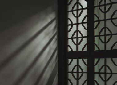 Güneş ışığı ince bir kafes tasarımı ile pencereden akar, duvarda uzamış gölgeler bırakır..