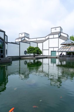 Suzhou, Çin - 12 Haziran 2024: Önünde gölet bulunan modern bir müze binası, sudaki binanın yansıması ve yüzen balıkların yansıması.