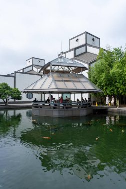 Suzhou, Çin - 12 Haziran 2024: Çatı penceresi olan modern bir pavyon, koi balıklarıyla çevrili küçük bir gölette bulunur..