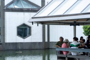 Suzhou, Çin - 12 Haziran 2024: Altıgen pencereli modern bir bina, gölün altında insanların oturduğu bir gölet..