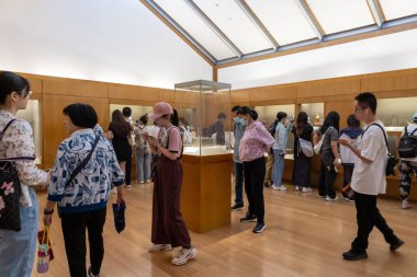 Suzhou, Çin - 12 Haziran 2024: İnsanlar ahşap zeminli ve kirişli beyaz tavanlı müzelerin içindeki eserlere bakıyorlar.