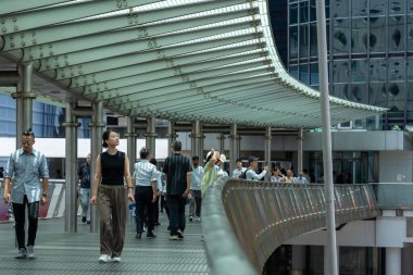 Hong Kong, Çin - 3 Temmuz 2024: İnsanlar metal bir gölgelik altında yürür ve Çin 'in Hong Kong kentindeki cam bir binanın önünden geçerler.