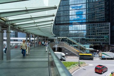 Hong Kong, Çin - 3 Temmuz 2024: Üzerinde çizgili bir tepe örtüsü ve üzerinde yürüyen insanlar olan bir yaya geçidi. Arkasında yansıtıcı pencereler olan gökdelenler. Yürüme yolunun manzarası işlek bir caddeye bakıyor..