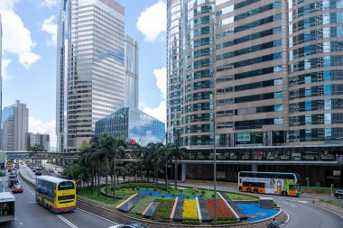 Hong Kong, Çin - 3 Temmuz 2024: Hong Kong, Çin 'de uzun gökdelenler, çift katlı otobüsler, palmiye ağaçları ve çiçeklerle dolu bir kavşak.