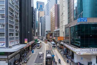 Hong Kong, Çin - 3 Temmuz 2024: Hong Kong, Çin 'de yoğun bir cadde, yol boyunca uzanan yüksek binalar. Bir sürü insan yürüyor ve araba sürüyor. Caddenin ortasında bir tramvay ve otobüs seferi görülebilir..