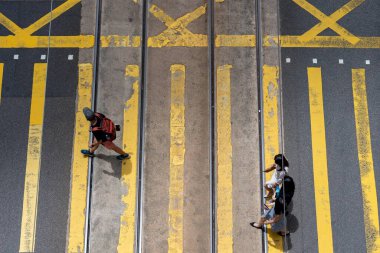 Hong Kong, Çin - 3 Temmuz 2024: Hong Kong, Çin 'de karşıdan karşıya geçen üç kişinin genel görünümü. Sokakta sarı çizgiler ve tramvay rayları var..