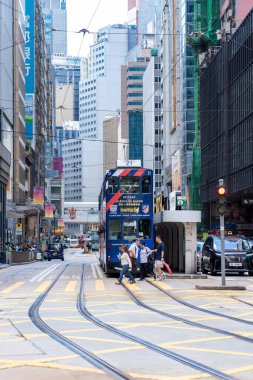 Hong Kong, Çin - 3 Temmuz 2024: Tramvay kalabalık bir Hong Kong şehrinde insanların caddeyi geçtiği ve arka planda binaların bulunduğu bir caddede durdu.
