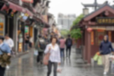 Çin 'deki Hangzhou caddesinde yürüyen insanların bulanık görüntüsü. Dükkanlar ve binalar cadde boyunca uzanır. Bokeh efektleri rüya gibi bir atmosfer yaratır..