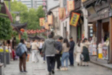 Çin 'in Hangzhou şehrinde sokakta yürüyen insanların bulanık bir görüntüsü. Her iki taraftaki binalar renkli pankartlar ve afişlerle süslenmiş ve sahne Bokeh tarafından daha da yumuşatılmış..