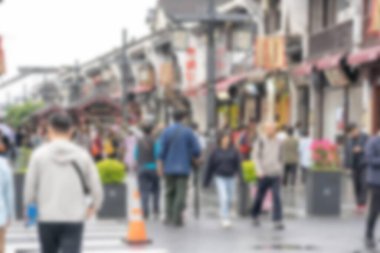 Çin 'in Hangzhou kentindeki bulanık bir sokak sahnesinde yayalar dükkanların önünden geçiyor ve bir trafik konisi....