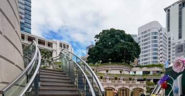 Hong Kong, Çin - 18 Eylül 2024: Geniş pencereli, saksılı ve büyük ağaçlı geleneksel bir binaya çıkan çelik parmaklıklı modern cam merdiven.