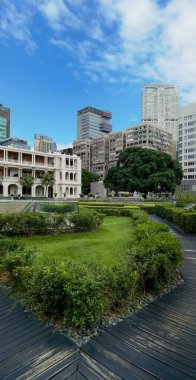 Hong Kong, Çin - 18 Eylül 2024: Ahşap yolu ve Hong Kong kentsel manzarası olan yeşil bir avlu.