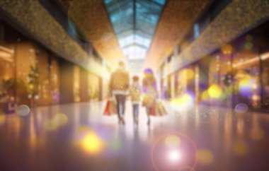 Alışveriş poşetleriyle bir alışveriş merkezinden geçen üç kişilik bir aile, mağazanın pencereleri festival dekorasyonlarının ışığını yansıtıyor. Bulanık arkaplan