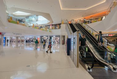 Shenzhen, Çin - 25 Ekim 2024: Yürüyen merdivenleri, beyaz fayansları ve uzayda yürüyen müşterileri olan modern bir alışveriş merkezi.