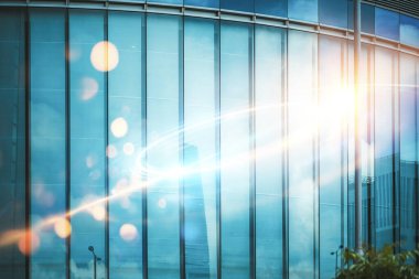 Büyük cam pencereli modern bir bina, güneşin parlaklığını yansıtır ve ışık çizgileri oluşturur..