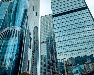 Hong Kong 'da yükselen gökdelenlerin yakın görüntüsü şehrin modern mimarisini ve kentsel yoğunluğunu yansıtıyor. Cam cepheler ışıkta parıldıyor.