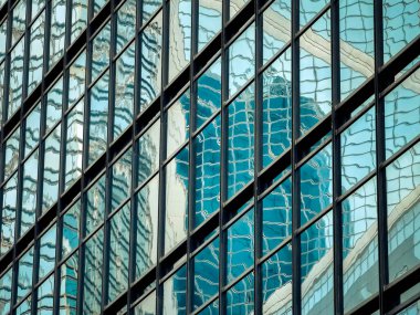 Bir Hong Kong binasının cam cephesini yakından görmek, şehri yansıtıyor. Pencerelerin ve yansımaların karmaşık ızgarası soyut bir şablon oluşturuyor.