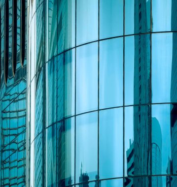 Şehrin ufuk çizgisini yansıtan modern bir Hong Kong binasının cam cephesinin yakın görüntüsü. Teal tonlu cam paneller çarpıcı bir görsel yaratıyor.
