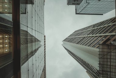 Hong Kong 'daki gökdelenlerin alçak açılı görüntüsü bulutlu bir gökyüzüne doğru uzanıyor. Şehrin yoğun mimarisi perspektif tarafından vurgulanıyor.