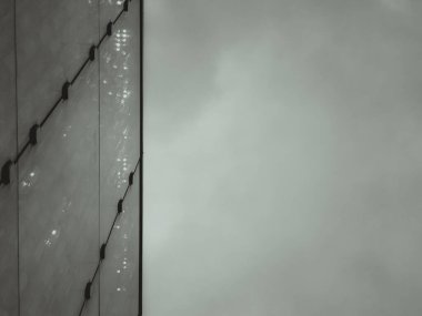 Hong Kong 'da modern bir binanın ön cephesine yakın çekim. Parlak metalik bir yüzey ve kısmen görülebilir cam bir yapı, sisli bir gökyüzüne karşı..