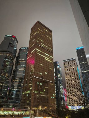 Hong Kong, Çin - 12 Mart 2025: Karanlık bir gece gökyüzüne karşı aydınlık gökdelenlerin alçak açılı görüntüsü. Işıklı yüksek binaların bulunduğu şehir manzarası. Alacakaranlıkta şehir manzarası.