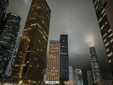 Hong Kong, Çin - 12 Mart 2025: Karanlık bir gökyüzüne karşı aydınlanan gökdelenlerle alçak açılı gece şehri. Bir metropoldeki yüksek binaların şehir manzarası.