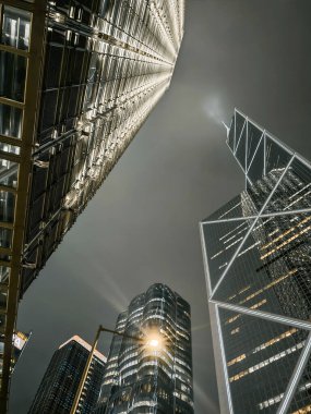 Hong Kong, Çin - 12 Mart 2025: Geceleri modern gökdelenlere bakıyorum. Işıklar yüksek binaları aydınlatıyor. Karanlık gökyüzüne karşı dramatik bir perspektif oluşturuyor..
