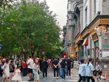 Pekin, Çin - 15 Eylül 2025: Pekin 'in tarihi Qianmen Caddesini dolduran kalabalık geleneksel binaları ve yeşil ağaçları dekoratif kırmızı fenerlerle geziyor.