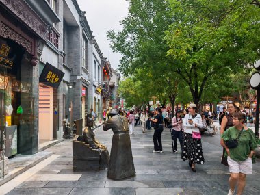 Pekin, Çin - 15 Eylül 2025: Pekin 'deki Bustling Qianmen Caddesi, canlı bir yaya bölgesi. Geleneksel mimari, yeşil ağaçlar ve bronz heykel sahneyi gösteriyor.
