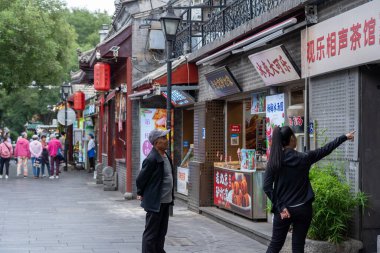 Sep 19, 2025 - Pekin, Çin: Beijing 'in tarihi Nanluoguxiang caddesinde bir satıcı, Hutongs' taki modern alışveriş sırasında gelenek sergiliyor.