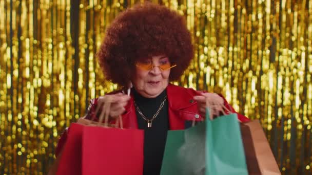 ショッピングバッグを示す緑豊かな髪を持つ幸せな観光の女性は 黒金曜日の休日に低価格のショッピングに驚いて見て笑顔割引広告 シニアスタイリッシュな祖母上の光沢のある背景 — ストック動画