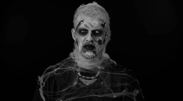 僵尸男子化妆假伤口疤痕和白色隐形眼镜看着相机 点击他的牙齿 试图吓唬在黑暗的房间 Sinister死的家伙 万圣节 舞台的概念 — 图库照片
