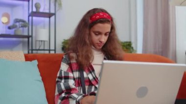 Preteen girl sit on couch closing laptop pc after finishing work in living room at home couch. Young child kid freelancer working online, remote job. E-learning, browsing internet on notebook computer