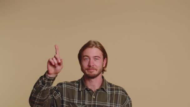 穿着衬衫的英俊男子竖起大拇指 指着空荡荡的地方 商业广告区 复制商品促销空间 年轻的成年人 在米色墙背景上拍摄的室内演播室 — 图库视频影像