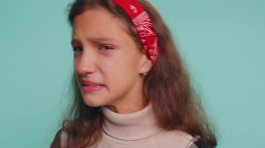 Hayal kırıklığına uğramış genç kız çocuk 12 yaşında gözyaşlarını siliyor ve umutsuzluktan ağlıyor. Haksız şeyler yüzünden üzgün olmak, kırık aşk. Stüdyo mavi arka planda izole edilmiş küçük çocuklar