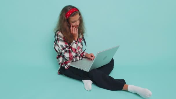 快乐的青少年小女孩12岁的时候在笔记本电脑上工作 发送消息 在网上购物 看电影 独自坐在工作室蓝色背景上的十几岁以下儿童 — 图库视频影像