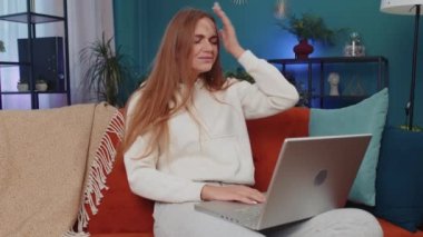 Portrait of caucasian adult girl use laptop typing browsing working, loses becoming surprised sudden lottery results, bad news, fortune loss, fail. Young woman sitting on orange couch at home room