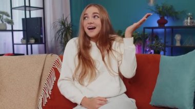 What. Why. Lovely girl raising hands in indignant expression, asking reason of failure, demonstrating disbelief irritation by troubles at home apartment. Young woman in room sitting on orange sofa