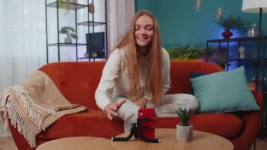 Kız blogcu cep telefonu kamerasından selfie çeken cihaza bakıyor, modern sosyal medya vlog uygulamasında sanal dans içeriği oluşturuyor. Akıllı telefonlu kadın sınıftaki kanepede oturuyor.