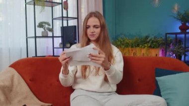 Stressed girl at home room looking at unpaid bank debt bills, doing paperwork, planning budget, calculate finances mortgage payments. Displeased young woman throws paper bills sitting on orange couch