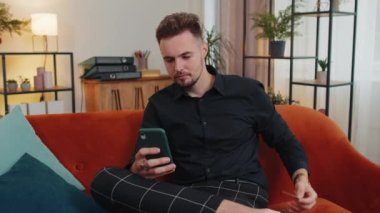 Modern ev apartmanında oturan ve çevrimiçi yemek siparişi veren, kredi kartı ile ödeme yapan mutlu tüketici genç adam. İnternette indirimli satış. Kanepede yetişkin bir adam.