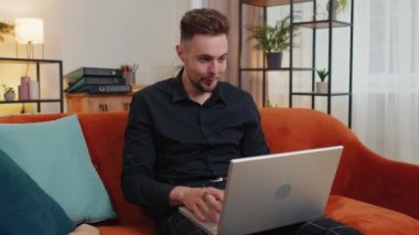 Memnuniyetle kanepede oturup dizüstü bilgisayar çığlığı atan beyaz adam zaferle el ele tutuşup başarıyı kutla piyangodan para kazan. Heyecanlı genç adam internette iyi haberler alıyor.