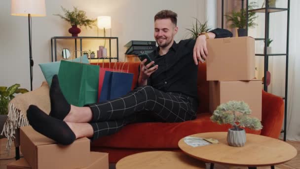 Happy Shopaholic Consumer Man Sitting Shopping Bags Modern Home Apartment — Stockvideo