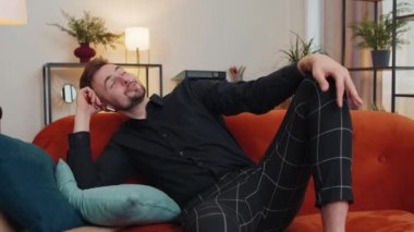 Kablosuz kulaklıklı genç adam evdeki koltukta uzanıyor ve en sevilen disko rock n roll müziğini kulaklıkla dinliyor. İnsanlar hafta sonu aktiviteleri. Çok mutlu bir adam
