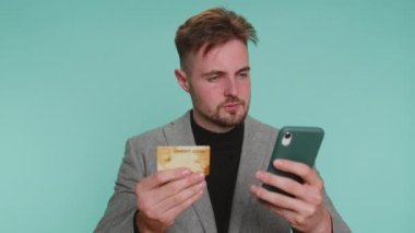 Para transferi, online alışveriş, ödeme yaparken kredi kartı ve akıllı telefon kullanan saygıdeğer bir iş adamı. Finans ve internet. Genç adam mavi duvarda tek başına kalmış.