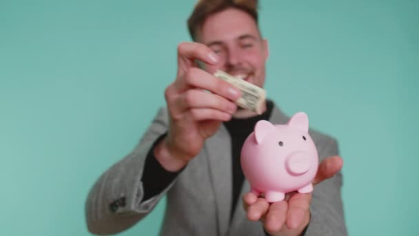 Счастливый Молодой Бизнесмен Предприниматель Экономит Деньги Используя Розовый Копилку Положить — стоковое видео